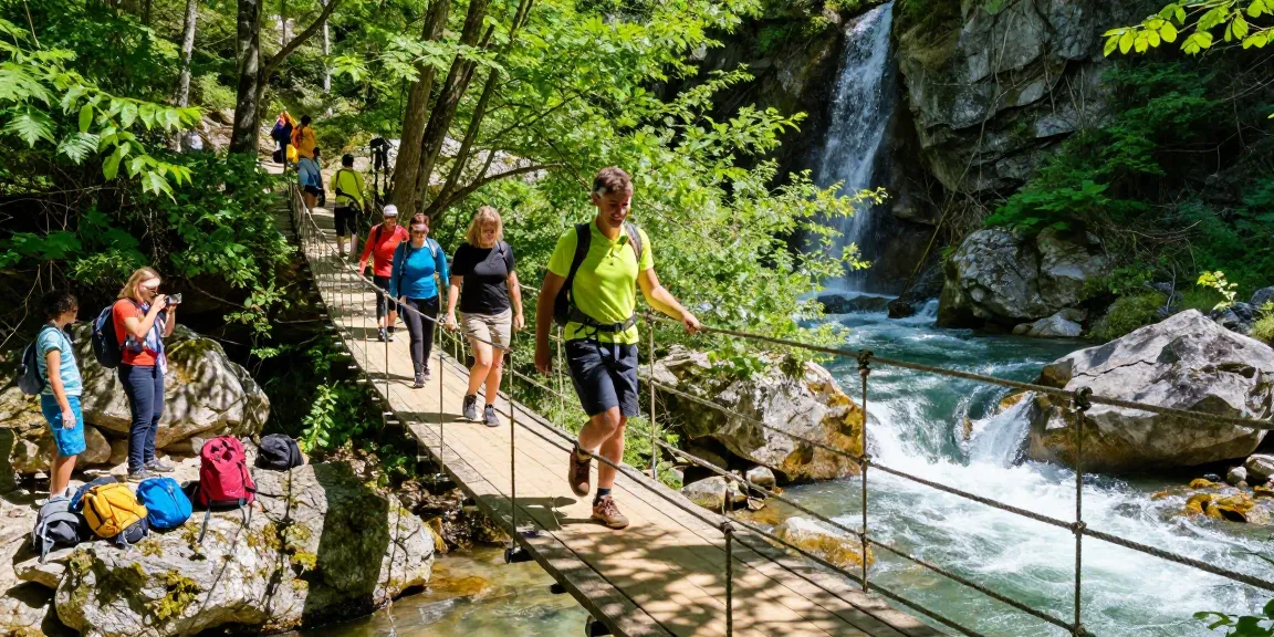 Group of hikers crossing a scenic River Rope Bridge surrounded by lush trees and a waterfall.